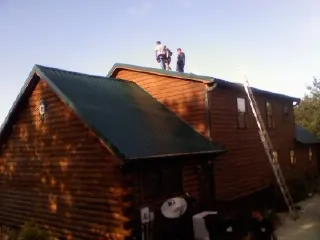 Crew on the ridge of a green metal roof on a two story log home in Holden