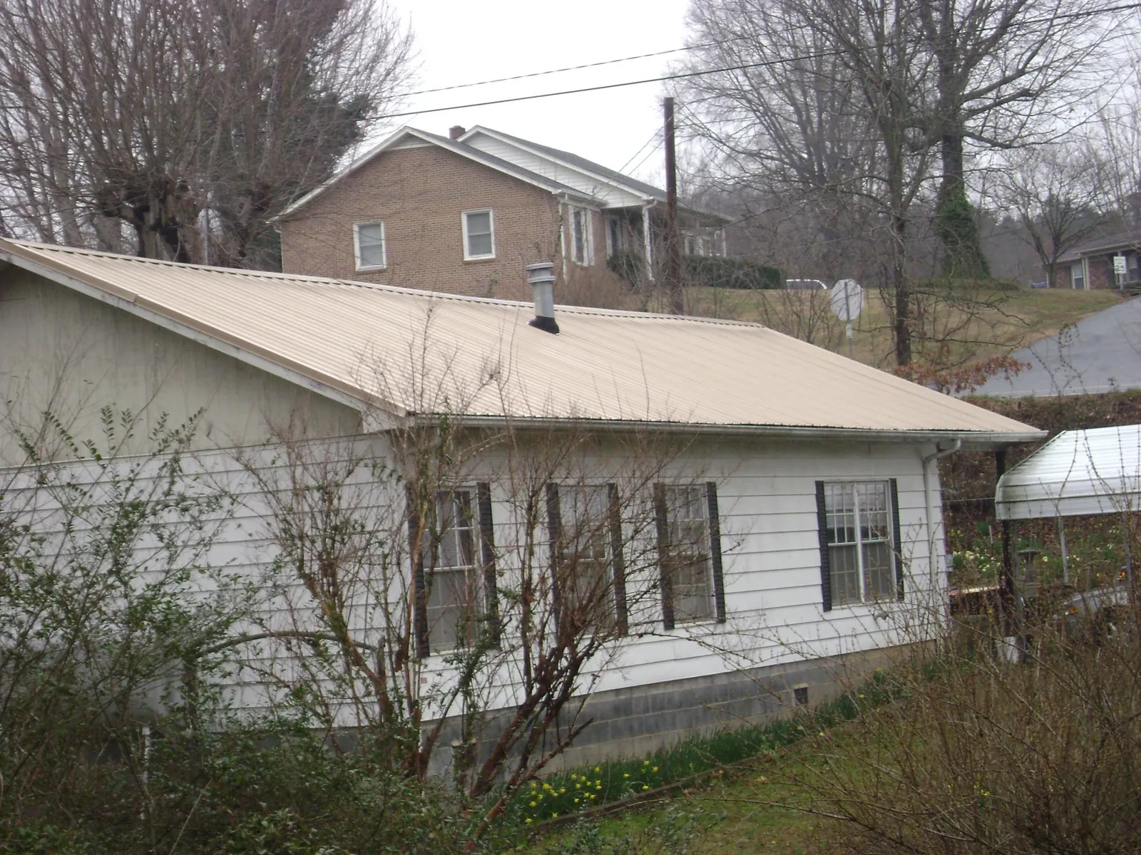 Tan metal roof on a white sided house set into a hillside — Commercial Roofing by Roofing Brothers in Holden